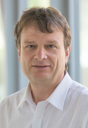 Herr Stauder trägt etwas wuschlige braune Haare und ein weißes Hemd