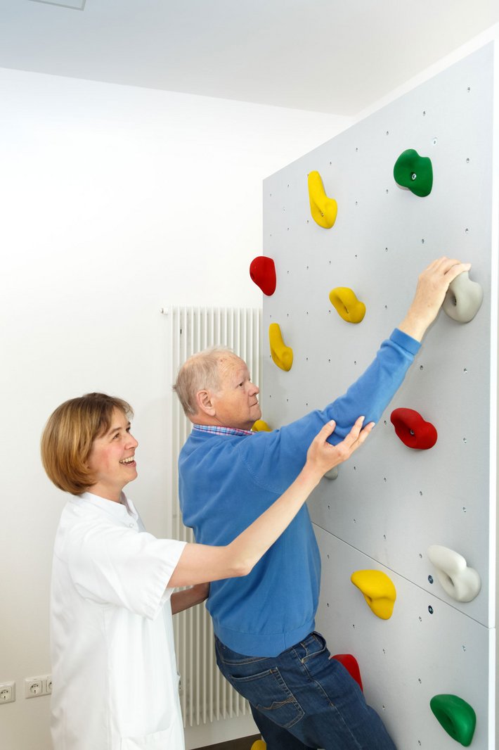 Unterstützt von einer Physiotherapeutin macht ein Patient Kletterübungen.