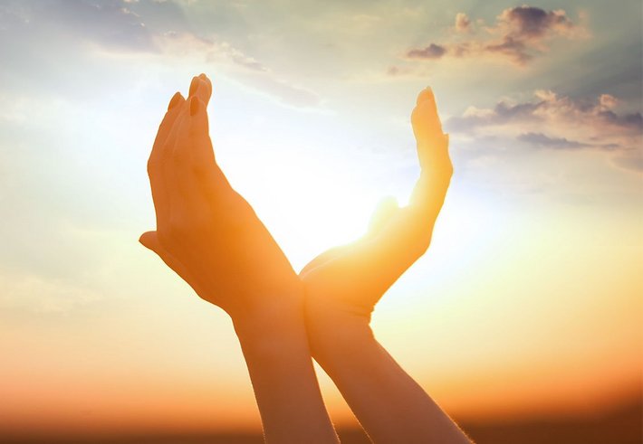 Zwei Hände formen bei Sonnenuntergang ein Herz.