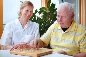 Ergotherapeutin Iris Stahl übt mit ihrem Patienten bei der Parkinsonkomplex-Behandlung am Steckbrett die Feinmotorik.