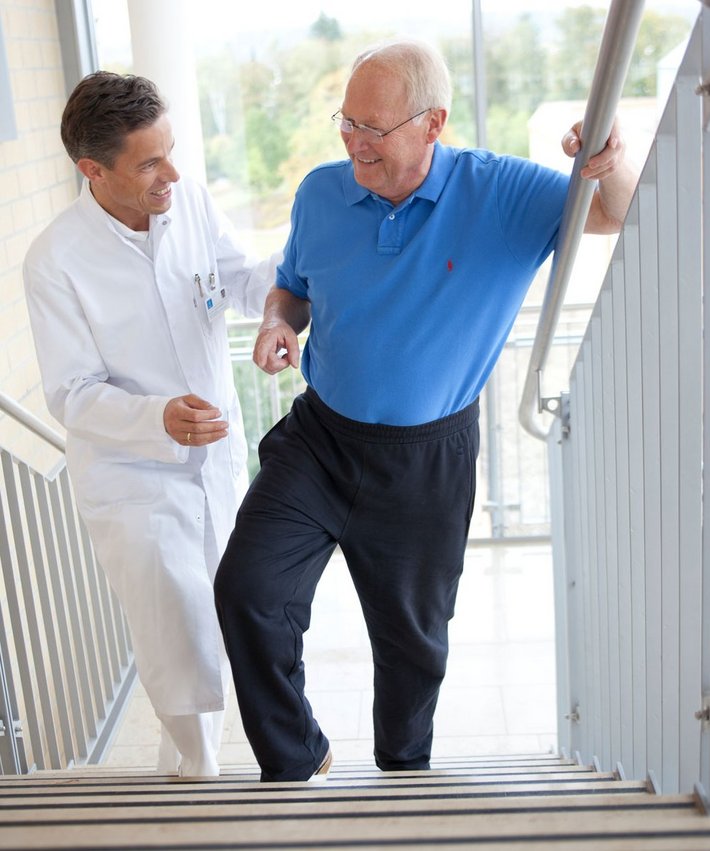 Patient und Arzt machen auf einer Treppe Übungen zur Mobilisierung nach einer Knie-OP