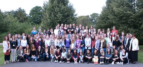 Man sieht 107 Azubis in einem Hof. Dahinter wachsen viele Bäume.