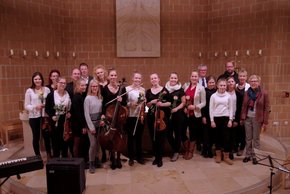 Die Schüler der Marienschule werden in einer Konzerthalle abgebildet. Sie halten ihre Instrumente, hauptsache Streichinstrumente, in den Händen.