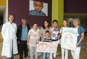 Man sieht den kleinen Patienten mit seinen Eltern, welche einen Scheck in den Händen halten. Zudem sind 3 Angestellte abgebildet.