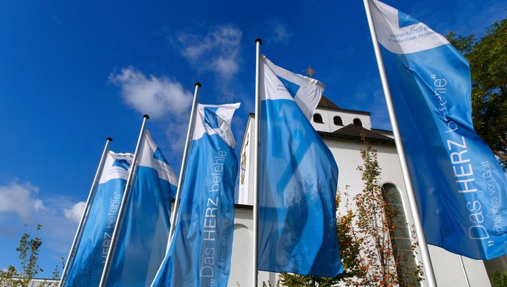 Die Fahnen am bei der Krankenhauskirche St. Pius tragen den Leitspruch des heiligen Johannes von Gott.