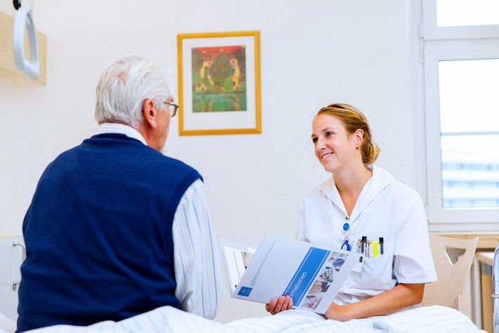 Pflegerin erklärt einem alten Patienten alles Wissenswerte um den Krankenhausaufenthalt