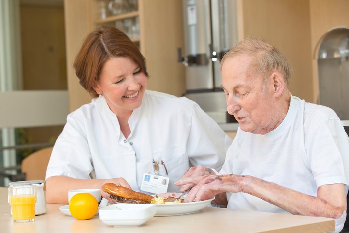 Alter Mann erhält Unterstützung beim Essen von einer Pflegerin